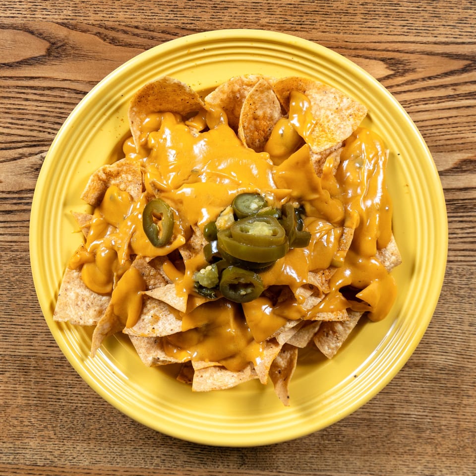 Fairweather nachos with melted cheese and sliced jalapeños on a yellow plate.