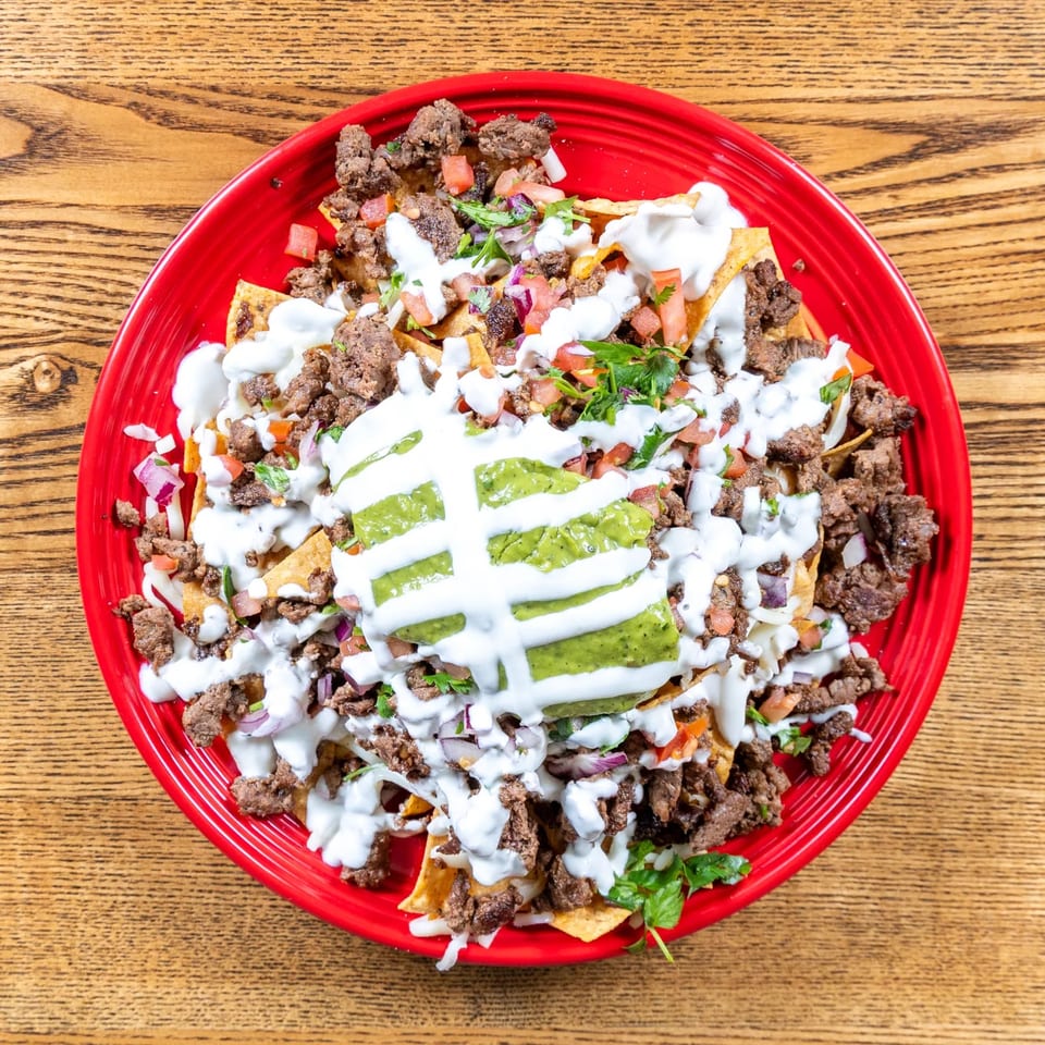 Fairweather's beef nachos with guacamole, sour cream, tomatoes, and onions on a red plate.