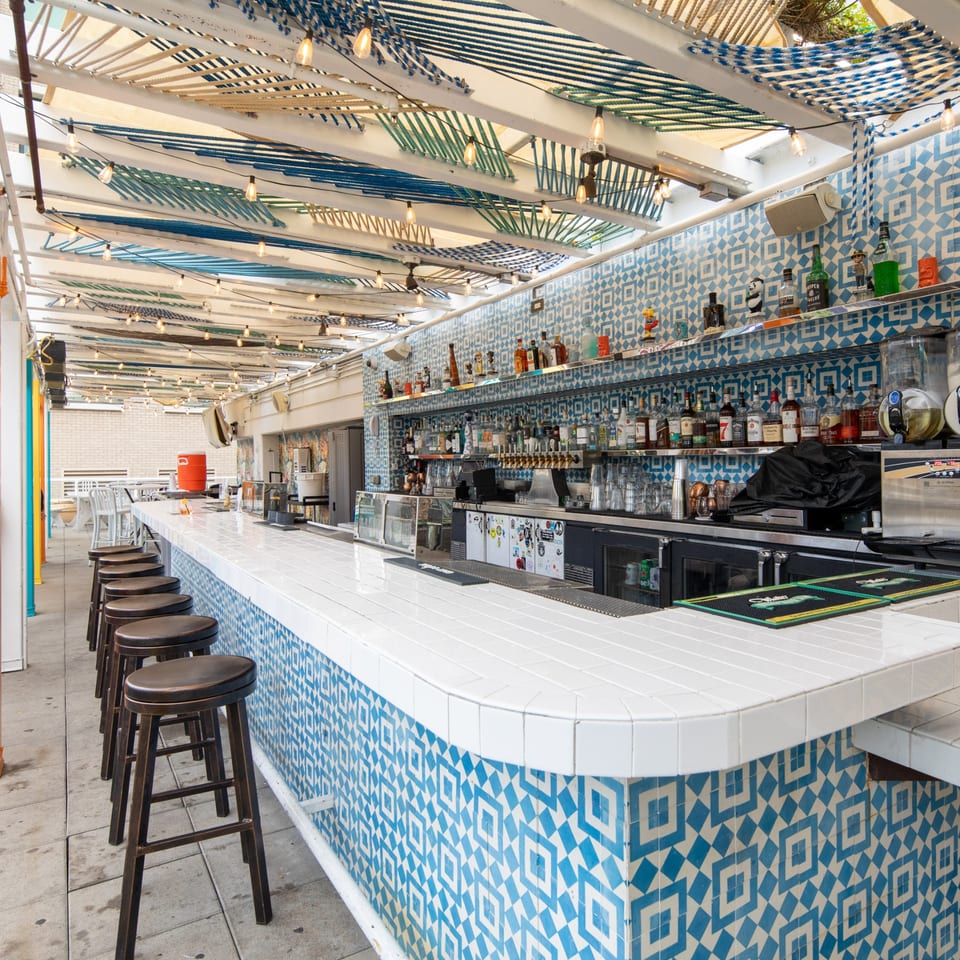 Fairweather bar with a white tiled counter, blue patterned base, and string lights overhead.