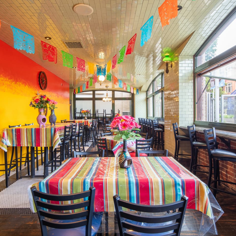 Fairweather bar interior with colorful striped tablecloths, floral centerpieces, and festive papel picado banners.