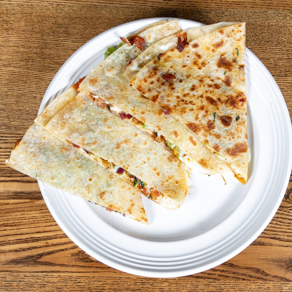 Golden-brown quesadillas, filled with melted cheese and other ingredients, served on a white plate.