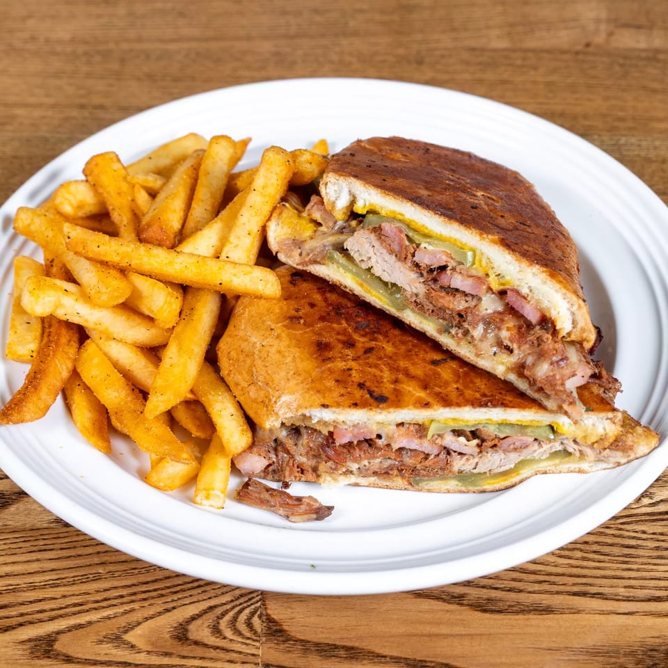 Fairweather's Cuban sandwich, cut in half, served with a side of golden french fries on a white plate.